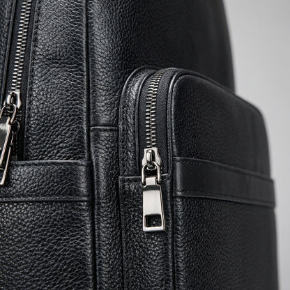 Close-up of a black leather backpack with zippers on a gray background